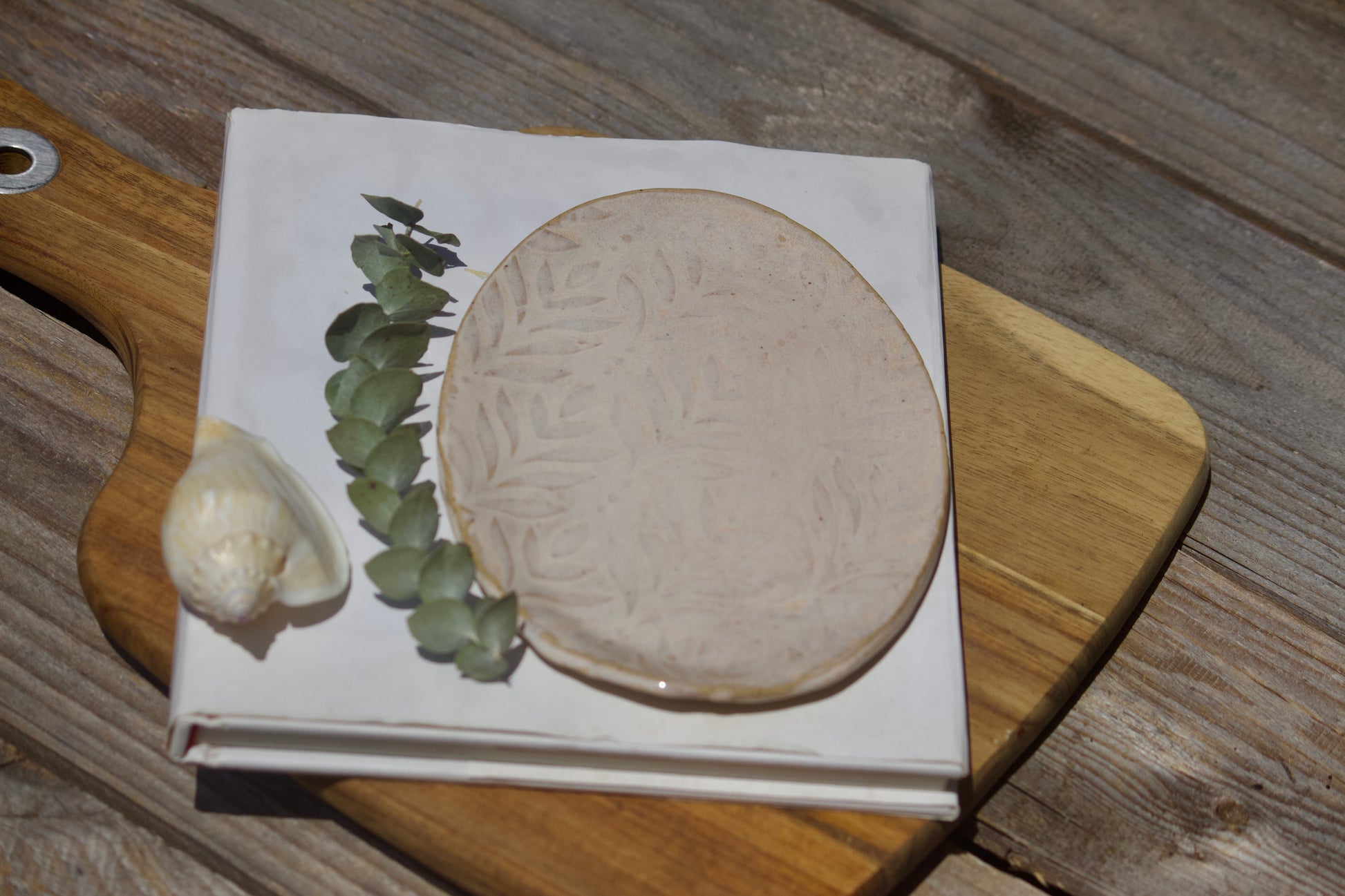 Handmade beige oval ceramic side plate with a textured lead design, displayed on a wooden surface.