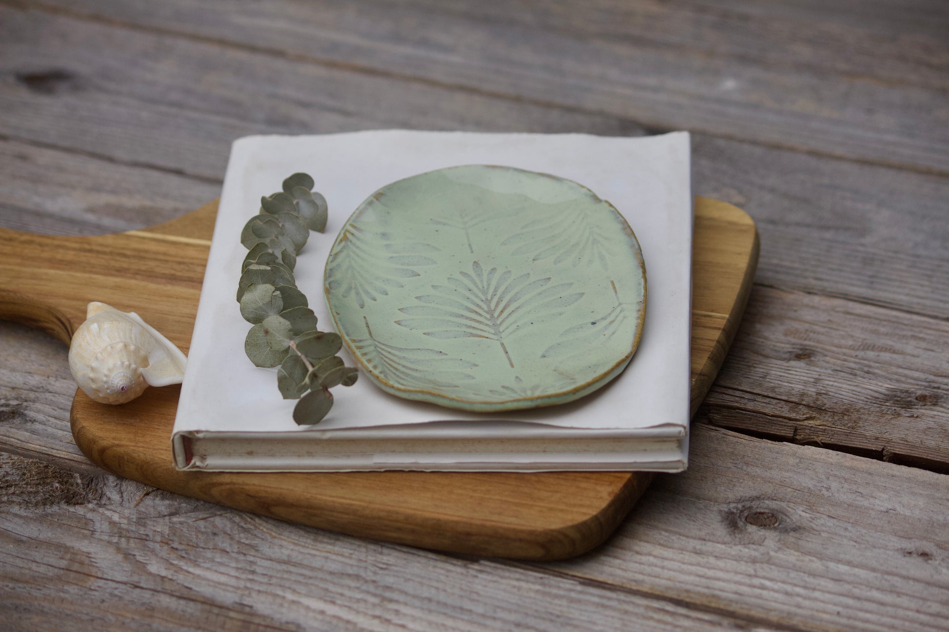 Green leaf ceramic side plate with textured design, displayed on white notebook and wooden board
