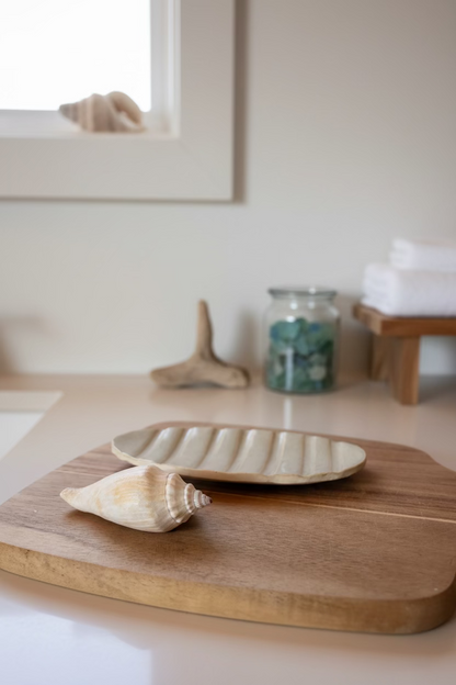 Wooden cutting board with a ceramic soap dish and shell on a light background
