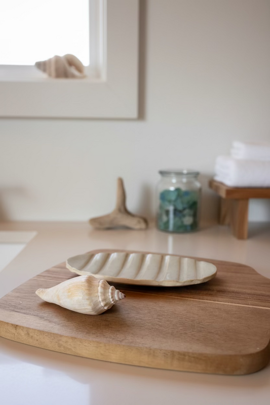Wooden cutting board with a ceramic soap dish and shell on a light background