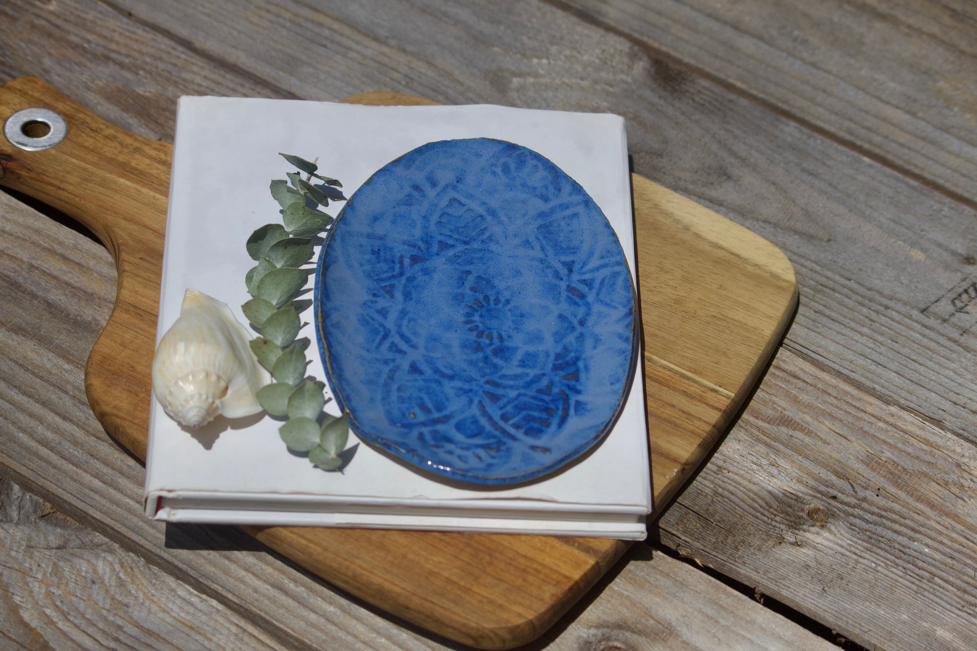Handmade oval ceramic side plate with a textured mandala design in indigo blue, displayed on a wooden surface.