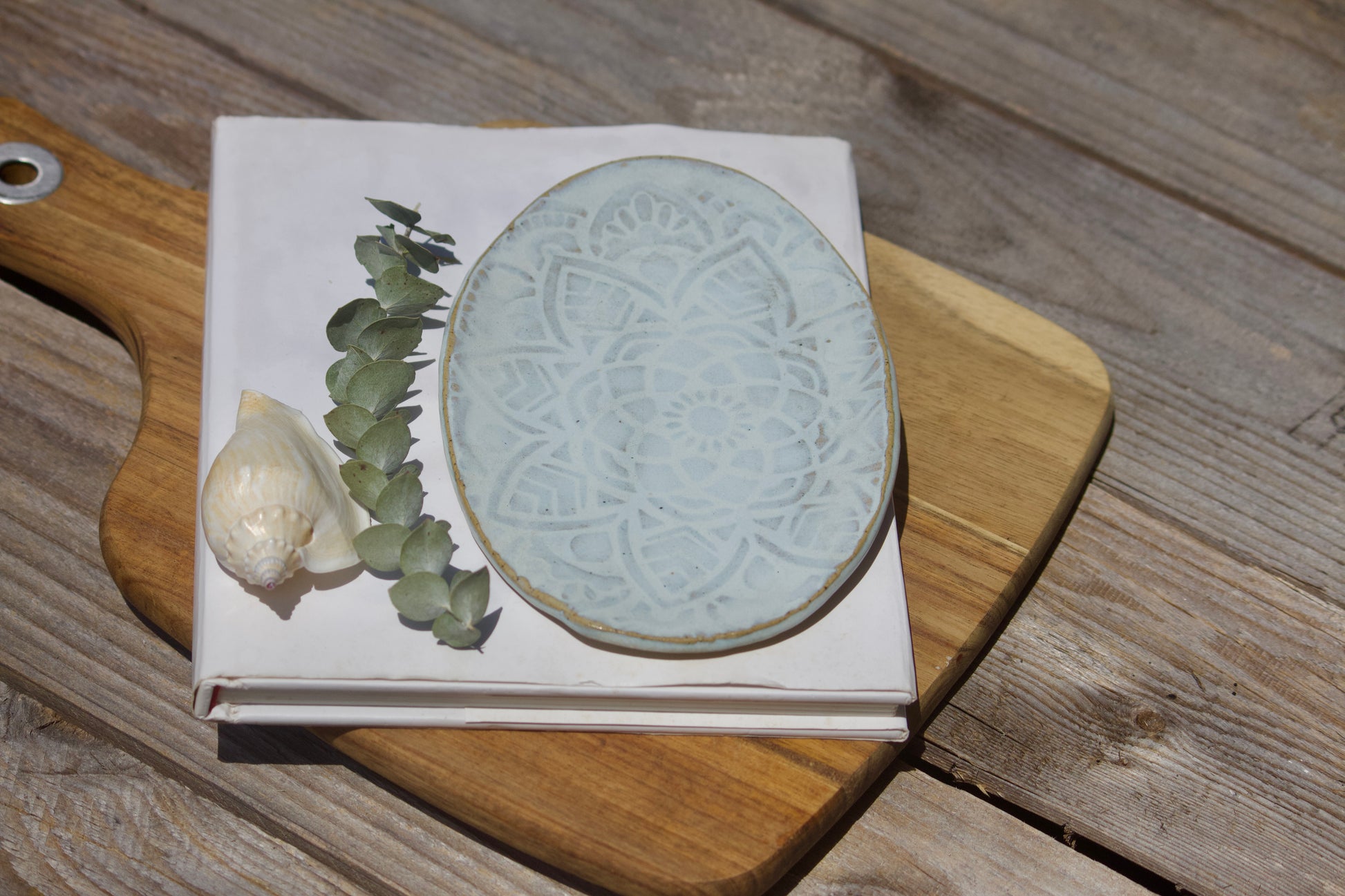 Handmade light blue oval ceramic side plate with a textured mandala design, displayed on a wooden surface.