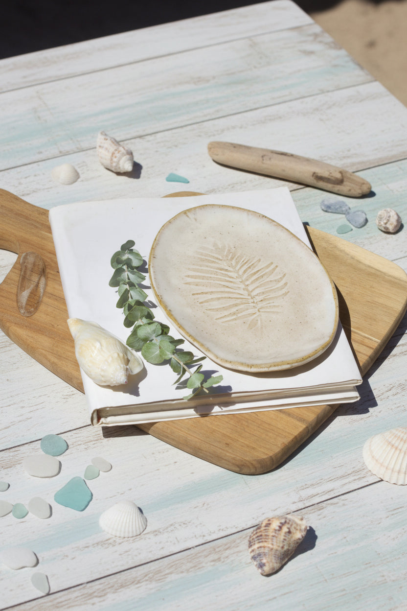 Handmade oval ceramic side plate with a textured plam design, displayed on a wooden surface.