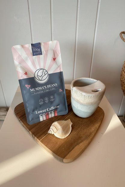 Mumma's Beans coffee packaging on a wooden surface with a ceramic travel mug and shell.